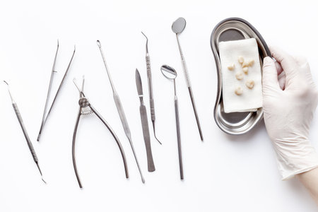 Dentist holding bowl with dental teeth crowns for dental prosthetics, top view. Dentist desk, white background.の写真素材