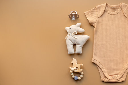 Flat lay with beige baby bodysuit and toys, top view. Newborn background.