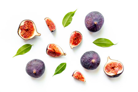 Fresh ripe figs whole and cut with green leaves on white background. Top view.の写真素材