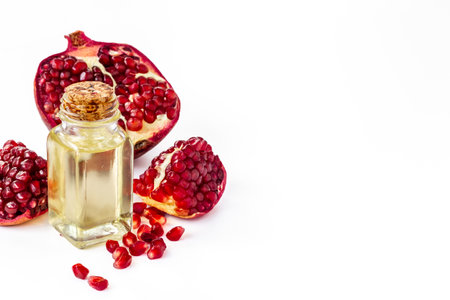 Pomegranate seed oil in a glass bottle and fresh fruit on a table, close up.の写真素材