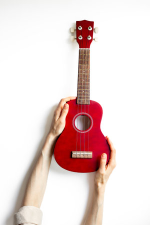 Hand is holding red small guitar ukulele. Musical instrument.