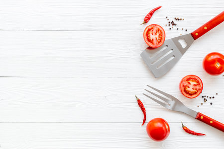 Picnic flatlay. Steel barbecue utensils with tomatoes and greens, top view.の写真素材