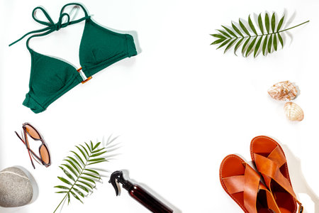 Stylish bikini swimsuit with sandals and tropical leaves, top view. Vacation beach accessories.の写真素材