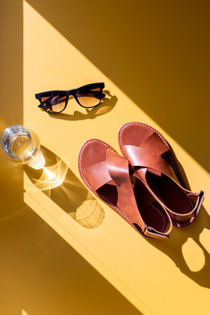 Sandals and sunglasses with sunlight on a yellow background, top viewの写真素材
