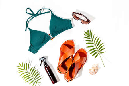 Vacation beach accessories with sunlight shadows. Stylish bikini swimsuit with sandals and tropical leaves, top view.の写真素材