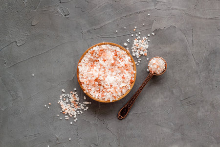 Coarse pink salt in wooden bowl and spoon and spilled salt. Cooking or spa concept.の写真素材