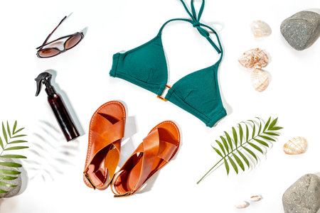 Vacation beach accessories with sunlight shadows. Stylish bikini swimsuit with sandals and tropical leaves, top view.の写真素材