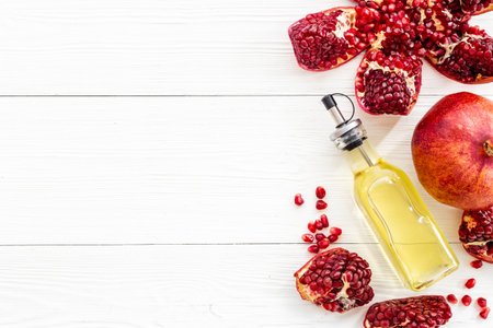 Glass bottle of pomegranate seed oil in a glass bottle and fresh fruit on a table, top view.の写真素材