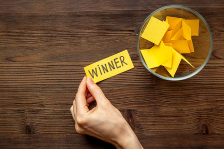 Hand is holding raffle ticket winner near glass jar, top view. Luck and lottery concept.の写真素材