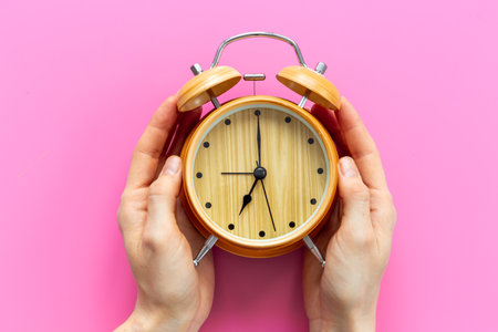 Hands are holding vintage wooden alarm clock with bells at seven o'clock. Morning routine. In time...