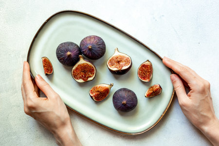 Hands are holding a plate with purple ripe figs and slices top view on a stone background.の写真素材