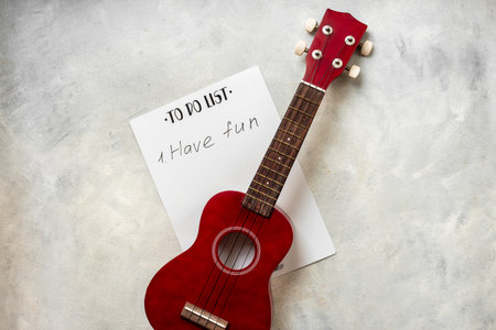 Small guitar ukulele on To do list with words Have fun. Musical instruments, top view.