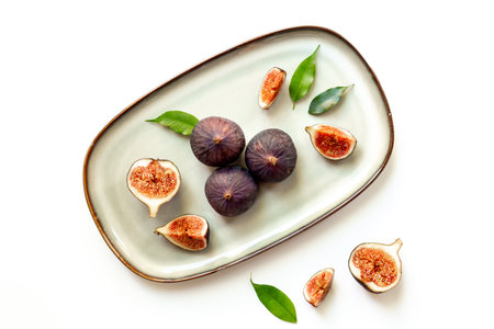 Purple ripe figs and slices with leaves on a plate top view on a white background.の写真素材