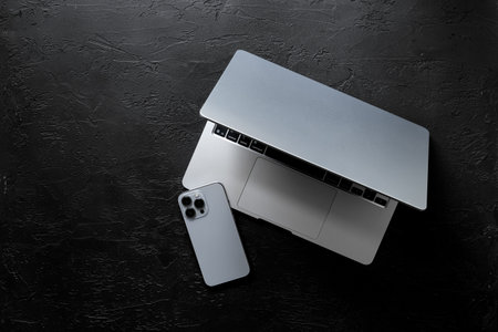 Silver laptop and mobile phone - high tech gadgets - on black stone background, top view.の写真素材