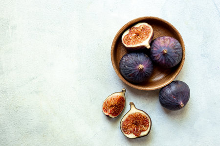 Fresh ripe figs on a wooden bowl top view on a stone background.