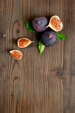 Purple ripe figs fruit and slices with green leaves top view on a wooden background.の写真素材