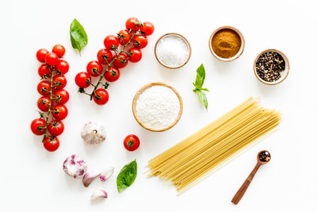 Spaghetti with ingredients for cooking Italian pasta - tomatoes and basil with garlic - on a white background, top view. Flat lay.の写真素材