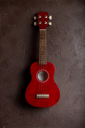 Red four string ukulele guitar, musical instrument, on brown background