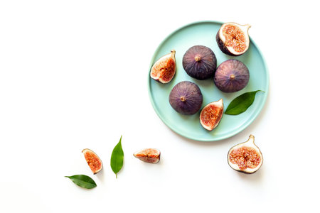 Purple ripe figs and slices with leaves on a plate top view on a white background.