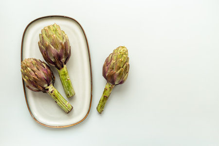 Three heads of purple artichokes on a plate top view. Vegetables ready to cook.の写真素材