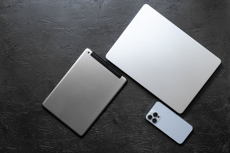 Silver laptop tablet and mobile phone - high tech gadgets on black stone background, top view