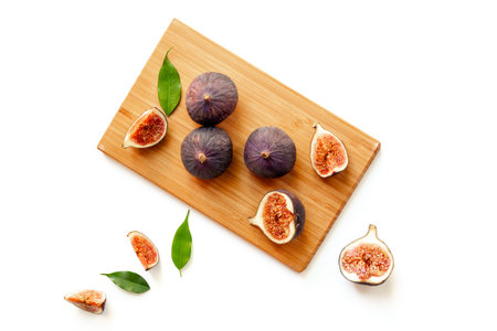 Purple ripe figs and slices with leaves on wooden bowl top view on a white background.