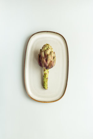 One artichoke flower - purple edible bud on a plate top view. Vegetables food ready to cook.の写真素材