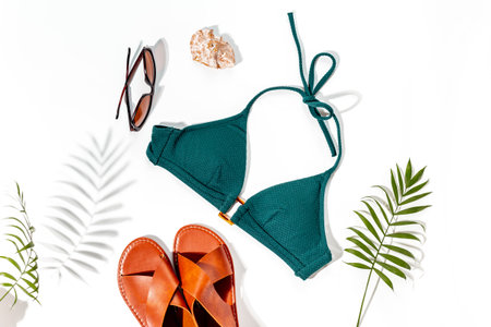Beach accessories with hard sunlight shadows - bikini swimsuit and tropical leaves, top view.の写真素材