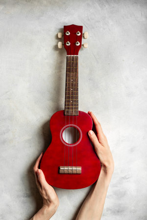 Hand is holding red small guitar ukulele. Musical instrument.