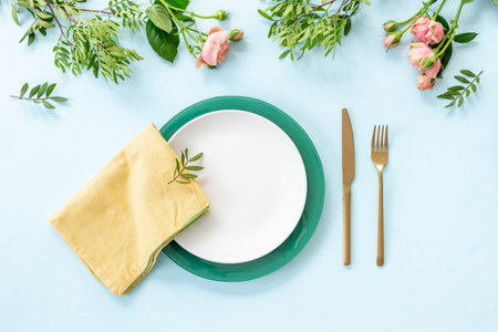 Top view of table setting with empty plate, cutlery and napkin - pink roses flowers decorated on blue background, flat layの写真素材