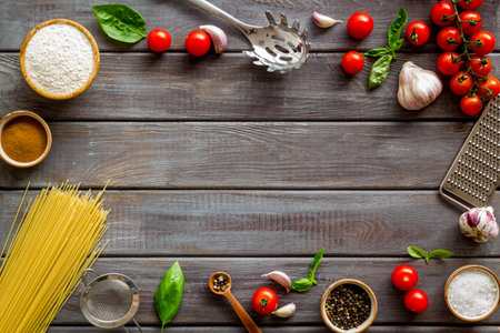 Frame of ingredients for cooking Italian pasta - uncooked spaghetti with tomatoes and basil leaves - on a wooden background, top viewの写真素材