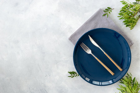Beautiful minimalistic table setting with empty plate, cutlery and napkin - green leaves decorated on gray stone background, flat lay. Top viewの写真素材