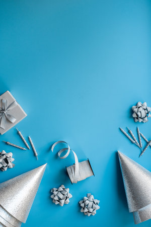 Frame of festive party decoration with silver streamers and gift box and carnaval caps on blue background, top view.の写真素材
