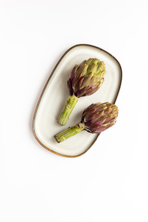 Purple artichokes flowers - edible buds on a plate top view. Vegetarian food ready to cook.の写真素材