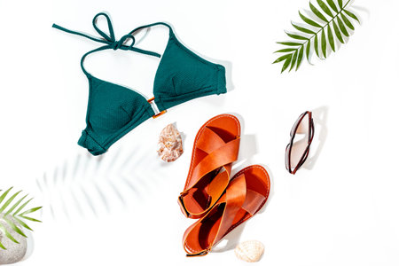 Stylish bikini swimsuit with sandals and tropical leaves, top view. Vacation beach accessories.の写真素材
