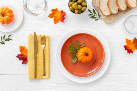 Festive Thanksgiving table setting with pumpkin and plate, cutlery and napkin - autumn leaves and tableware decorated on white wooden background, flat lay. Top view.の写真素材