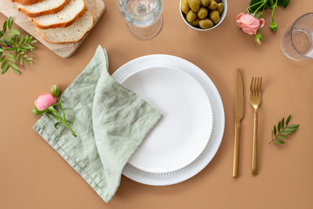 Festive table setting with empty plate, cutlery and napkin - flowers decorated, bread and olives for dinner, flat lay. Top view.の写真素材