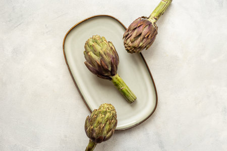 Tree heads of purple artichokes on a plate top view. Vegetables food ready to cook.の写真素材
