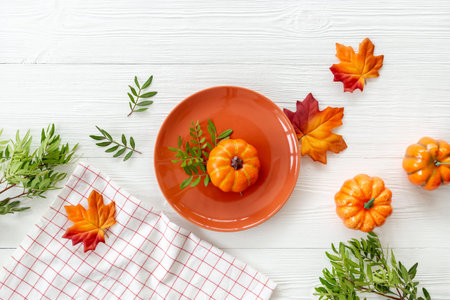 Top view of festive Thanksgiving table setting with pumpkin in plate and napkin - autumn leaves decorated on white wooden background, flat lay.の写真素材