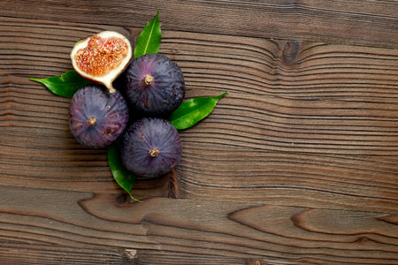 Purple ripe figs fruit and slices with green leaves top view on a wooden background.の写真素材