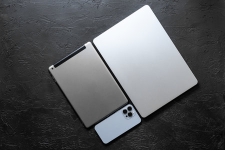 Silver laptop with tablet and mobile phone - high tech gadgets on black stone background, top view.の写真素材