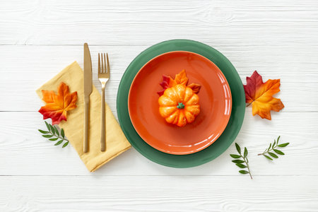 Top view of festive Thanksgiving table setting with pumpkin in plate, cutlery and napkin - autumn leaves decorated on white wooden background, flat lay.の写真素材