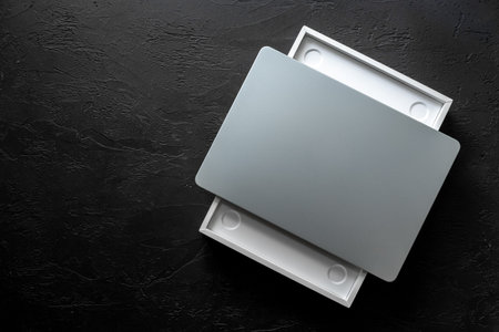 Silver laptop in a box on black desk top. Unpacking new gadget, top view.