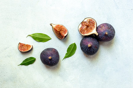 Purple ripe figs fruit and slices with green leaves top view on a stone background.