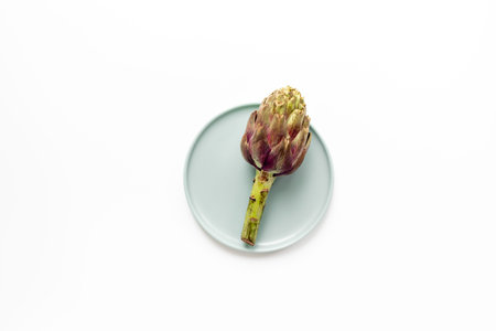One artichoke flower - purple edible bud on a plate top view. Vegetables food ready to cook.の写真素材