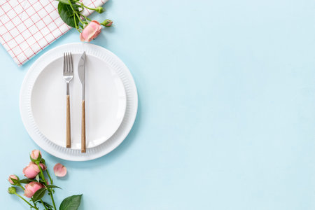 Top view of table setting with empty plate, cutlery and napkin - pink roses flowers decorated on...