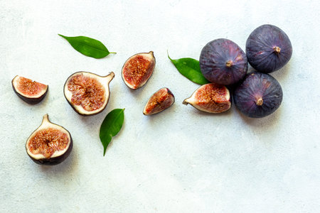 Purple ripe figs fruit and slices with green leaves top view on a stone background.