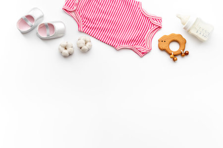 Flat lay of baby accessories - bodysuit and boots with wooden teether toys and bottle of milk on white background, top view.の写真素材