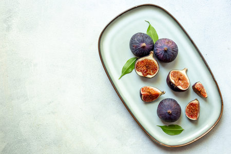 Purple ripe figs and slices with leaves on a plate top view on a stone background.
