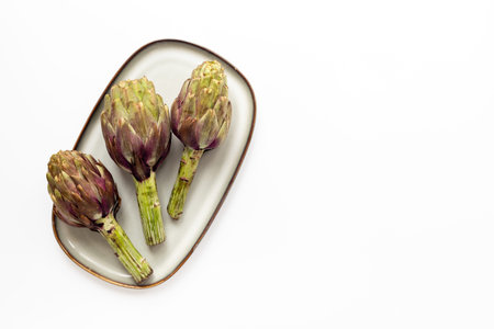 Three artichokes flowers - purple edible buds on a plate top view. Vegetarian food ready to cook.の写真素材